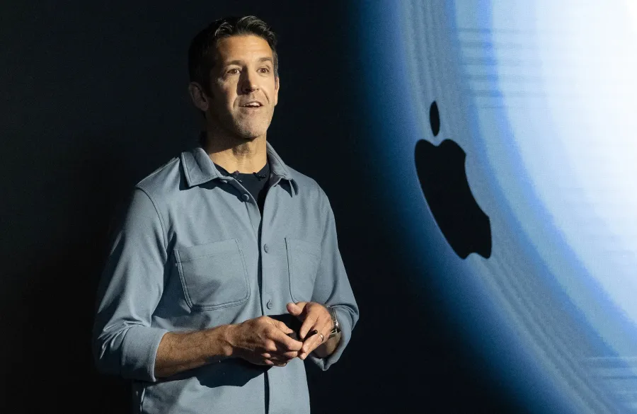 John Ternus, Senior Vice President of Hardware Engineering, presenting at an Apple event against an Apple logo backdrop