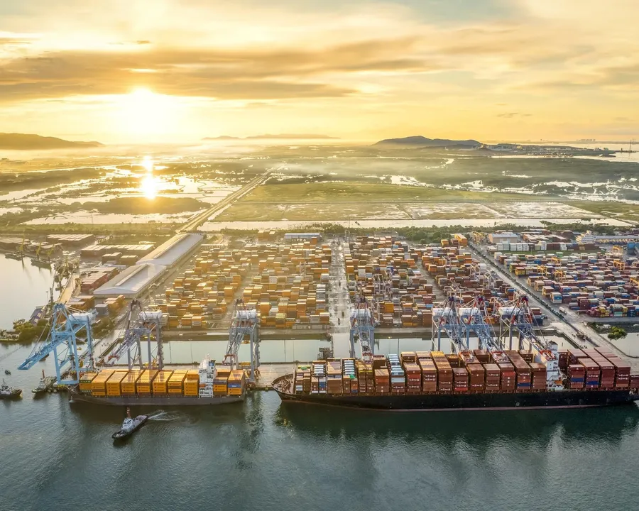 A container port with cargo ships unloading at sunset